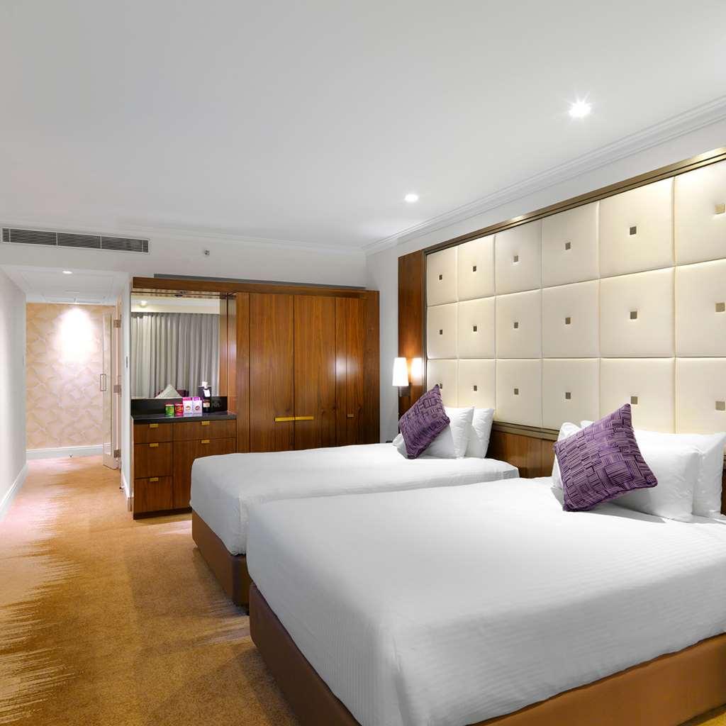 Amora Hotel Jamison Sydney Bilik gambar The photo shows a modern hotel room featuring two twin beds with white bedding and purple decorative pillows. The walls are designed with soft beige panels, creating a luxurious ambiance. There’s wooden furniture, including a cabinet against one wall
